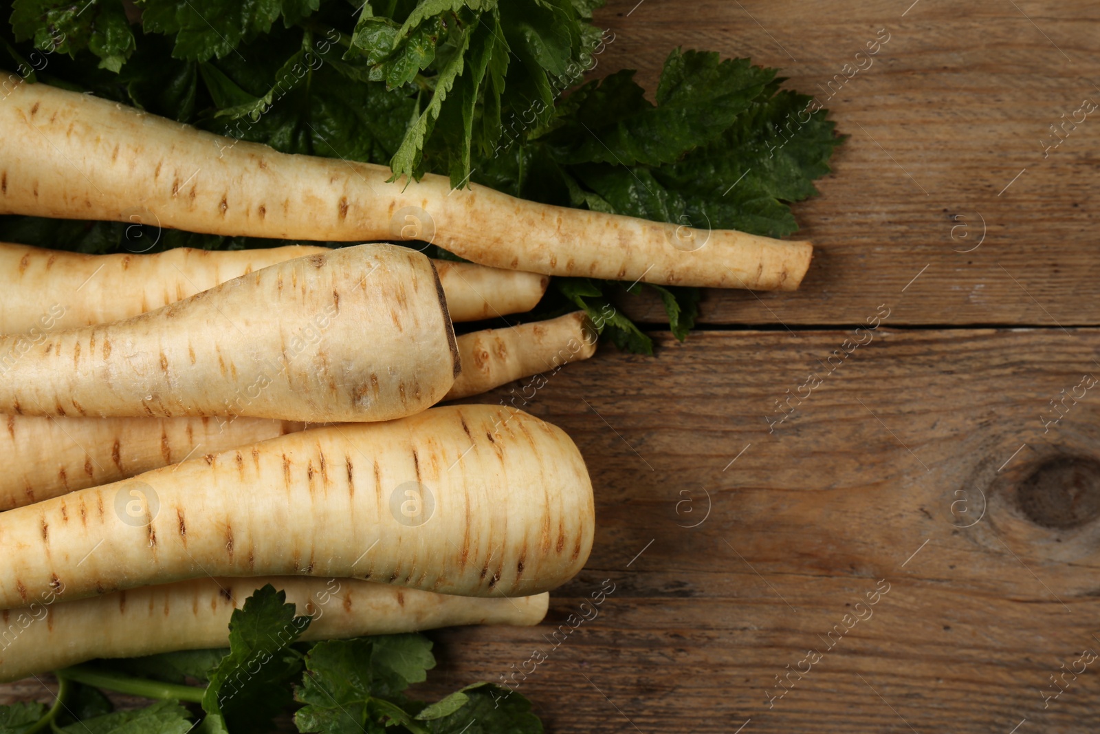 Photo of Fresh ripe parsnips with leaves on wooden table, flat lay. Space for text