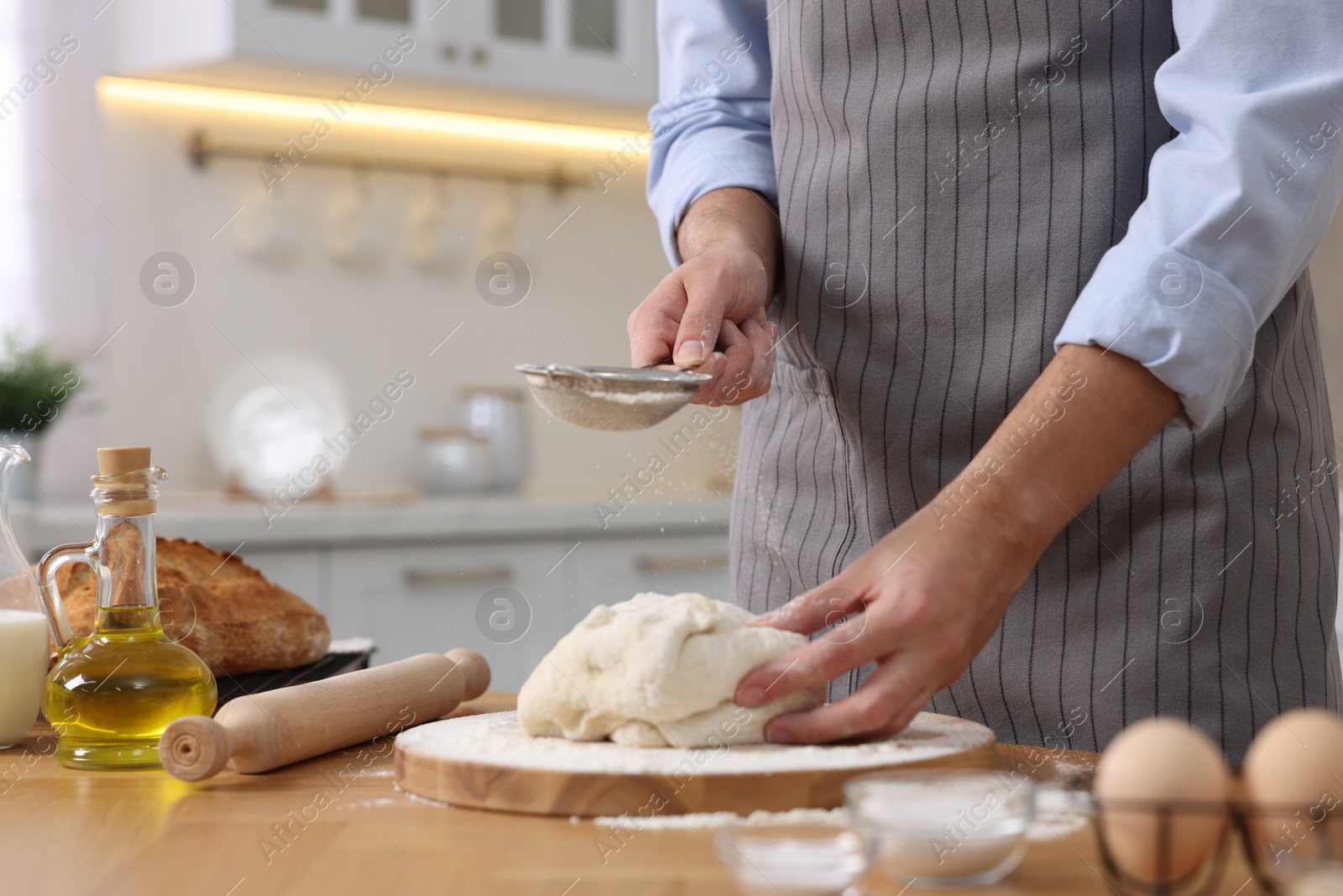 Photo of Making bread. Man sprinkling flour onto dough at wooden table in kitchen, closeup