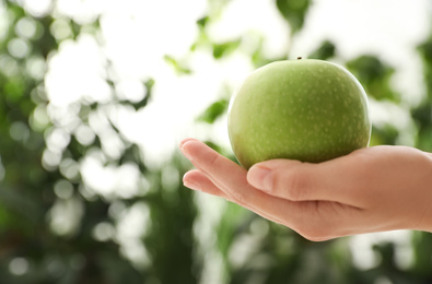 Photo of Woman holding fresh ripe green apple against blurred background, closeup. Space for text