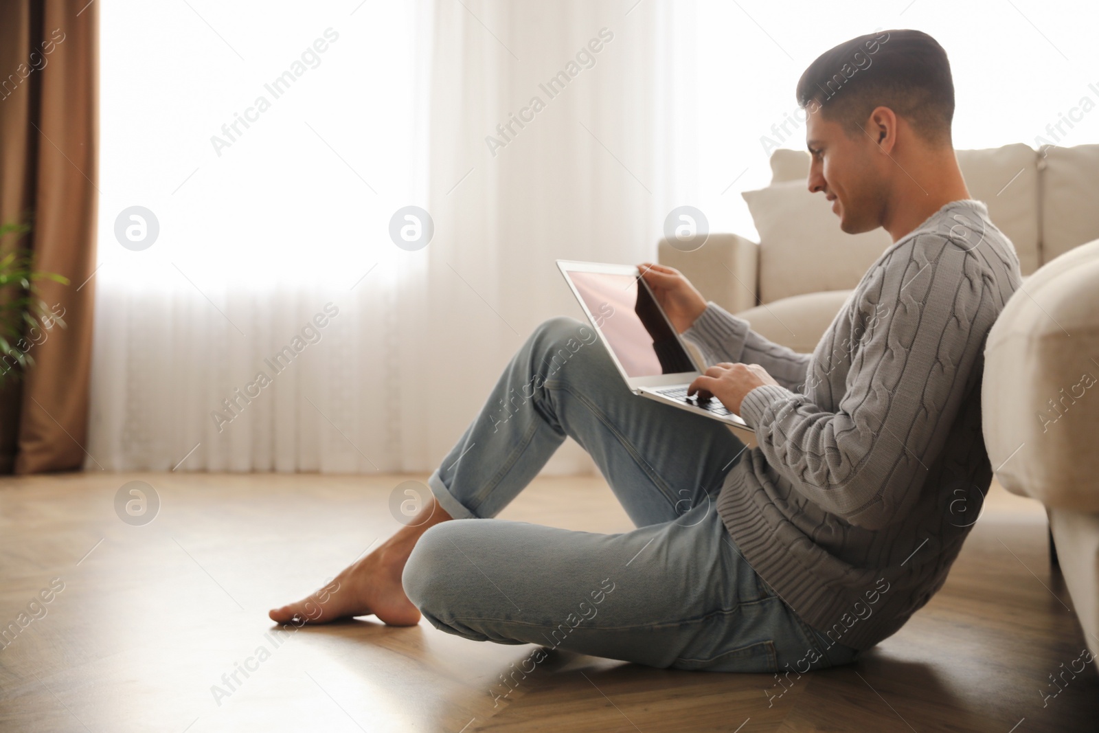 Photo of Man with laptop sitting on warm floor in living room. Heating system