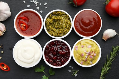 Photo of Different tasty sauces in bowls and ingredients on black table, flat lay