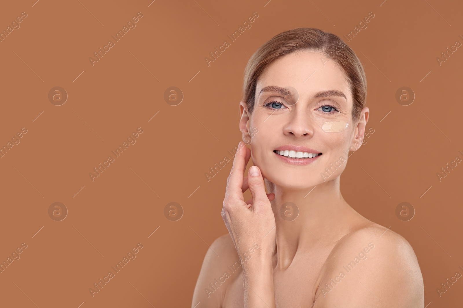 Photo of Woman with swatch of foundation on face against brown background. Space for text