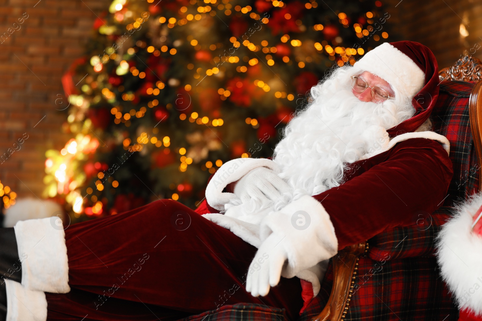 Photo of Santa Claus resting in armchair near decorated Christmas tree indoors