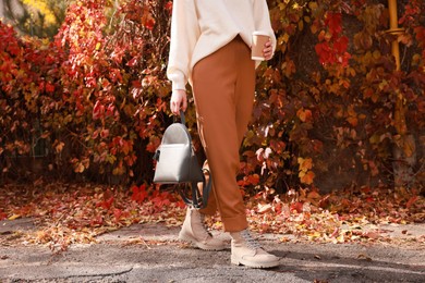 Photo of Young woman with stylish grey backpack and hot drink in autumn park, closeup