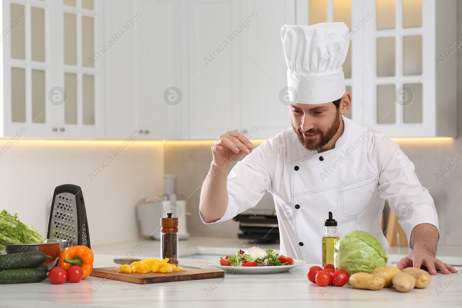 Photo of Professional chef salting delicious salad at marble table in kitchen. Space for text