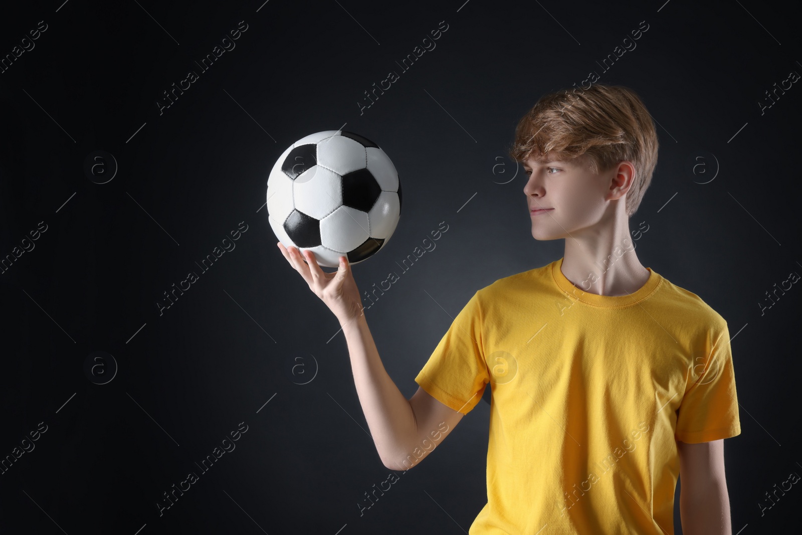 Photo of Teenage boy with soccer ball on black background. Space for text