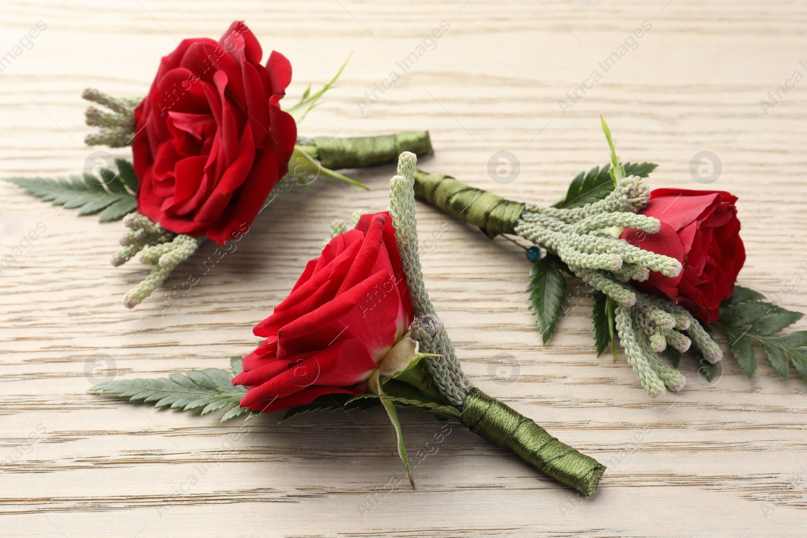 Photo of Many stylish red boutonnieres on light wooden table