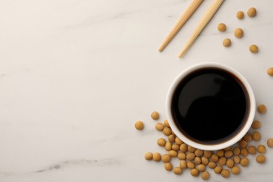 Photo of Soy sauce in bowl, soybeans and chopsticks on white marble table, flat lay. Space for text