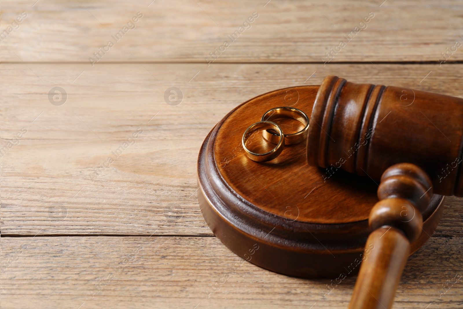 Photo of Divorce process. Gavel and wedding rings on wooden table, closeup. Space for text