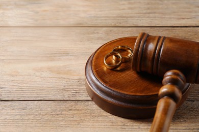 Photo of Divorce process. Gavel and wedding rings on wooden table, closeup. Space for text