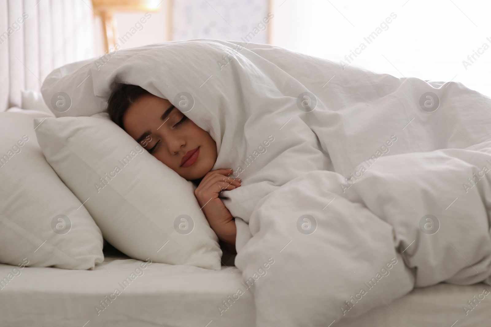 Photo of Young woman covered with warm white blanket sleeping in bed at home