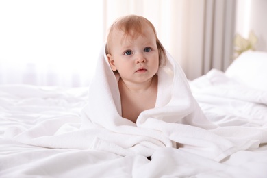 Cute little baby with soft towel on bed after bath