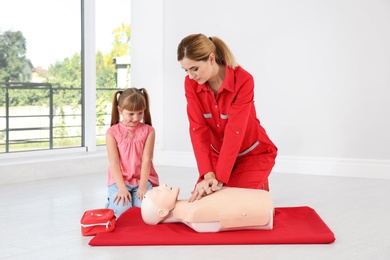 Instructor with little girl practicing first aid on mannequin indoors