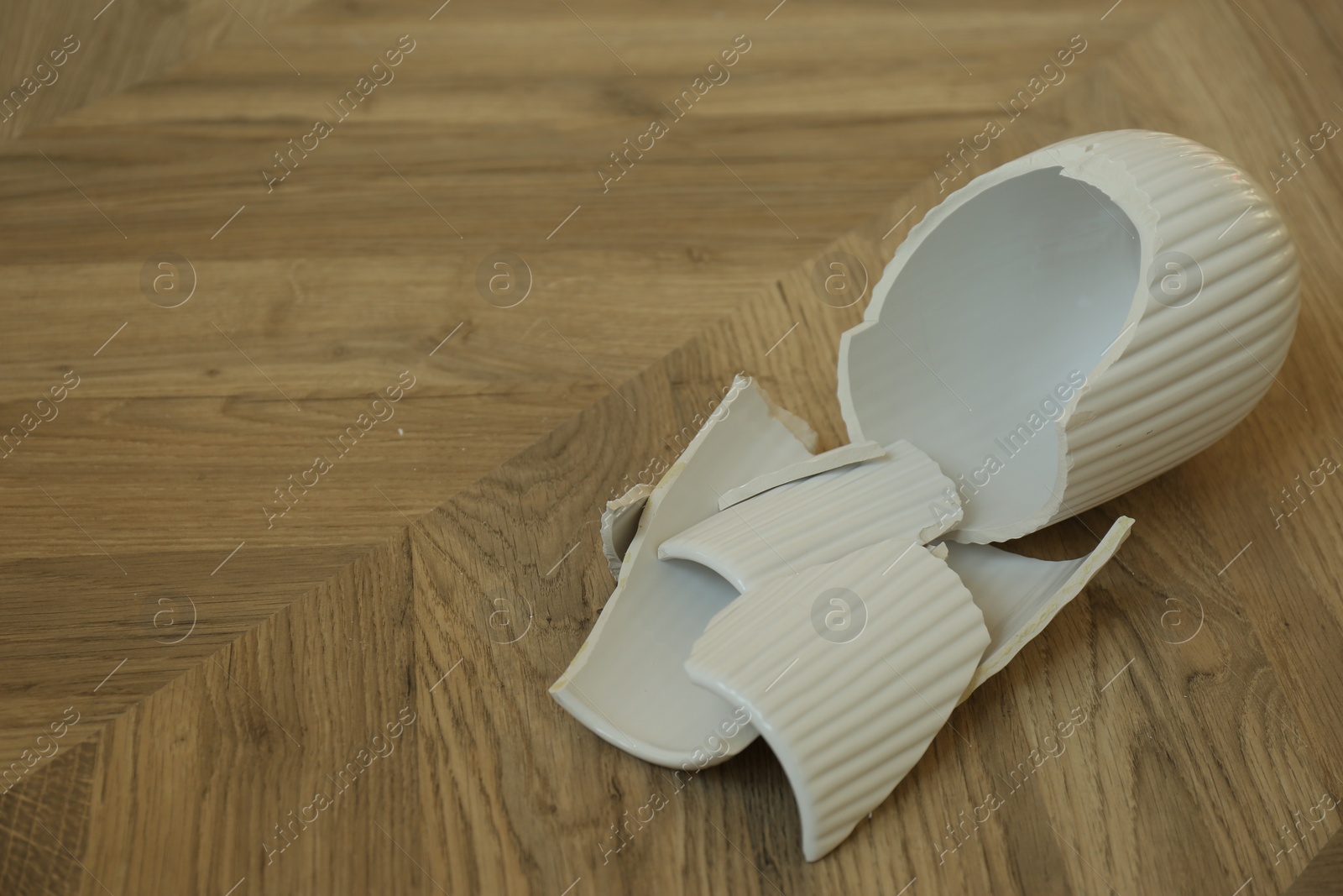 Photo of Broken white ceramic vase on wooden floor. Space for text