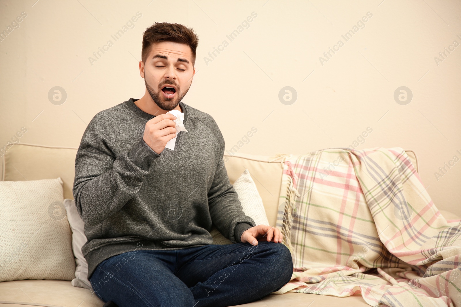 Photo of Sick young man sneezing at home. Influenza virus