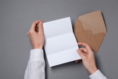 Photo of Woman with blank paper sheet at grey table, top view. Space for text