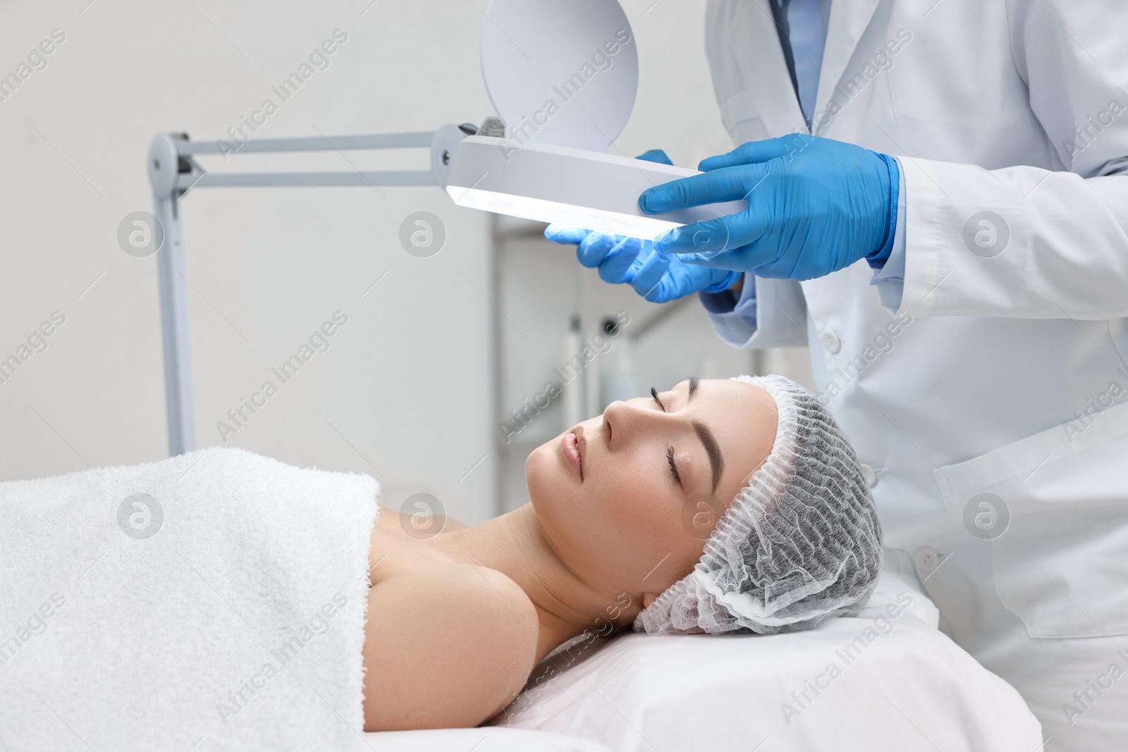 Photo of Dermatologist examining patient`s face under lamp in clinic, closeup