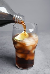 Photo of Pouring refreshing soda drink into glass on table against grey background