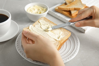 Photo of Woman spreading butter onto bread with knife over grey table, closeup