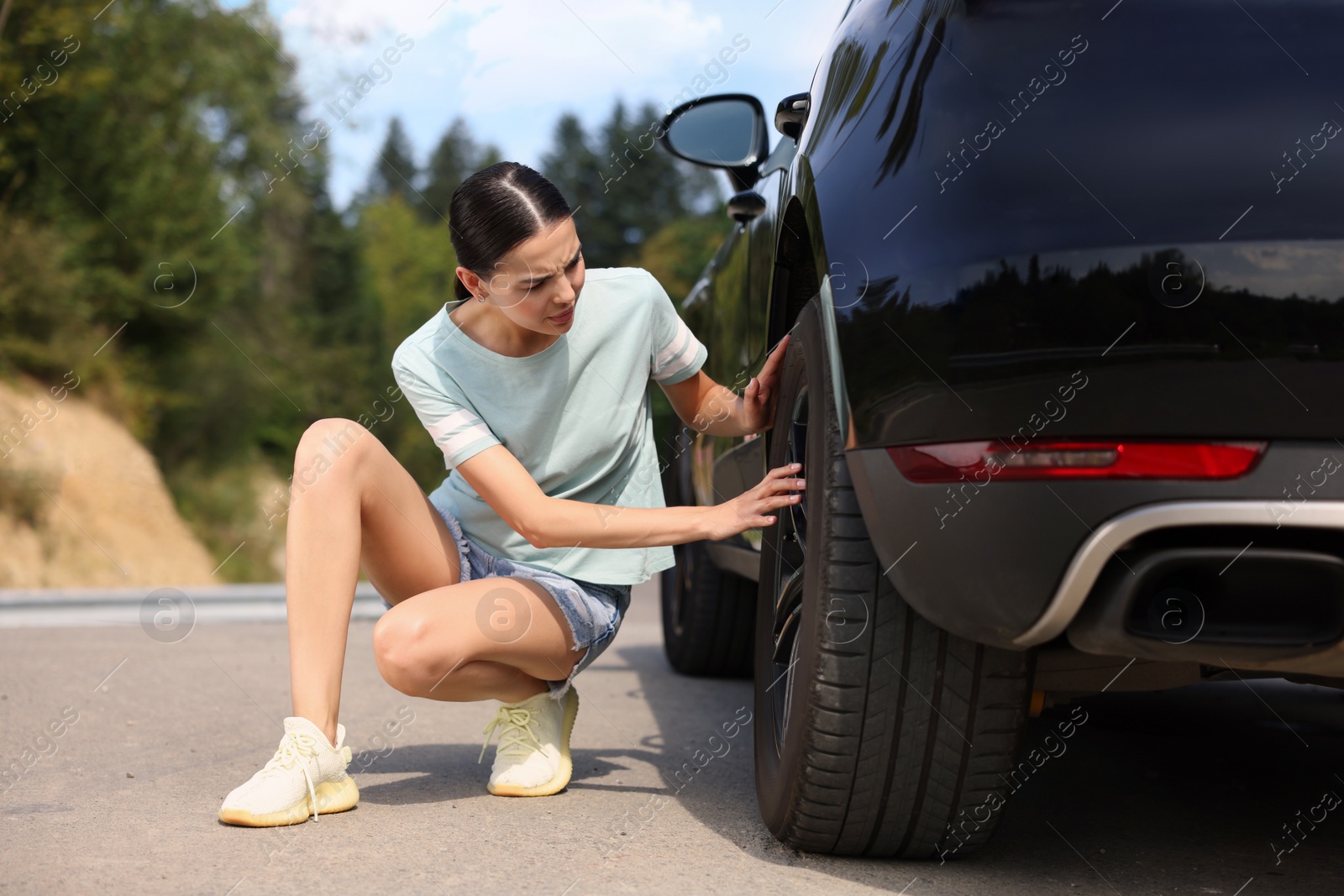 Photo of Tire puncture. Stressed woman checking wheel of car on roadside outdoors