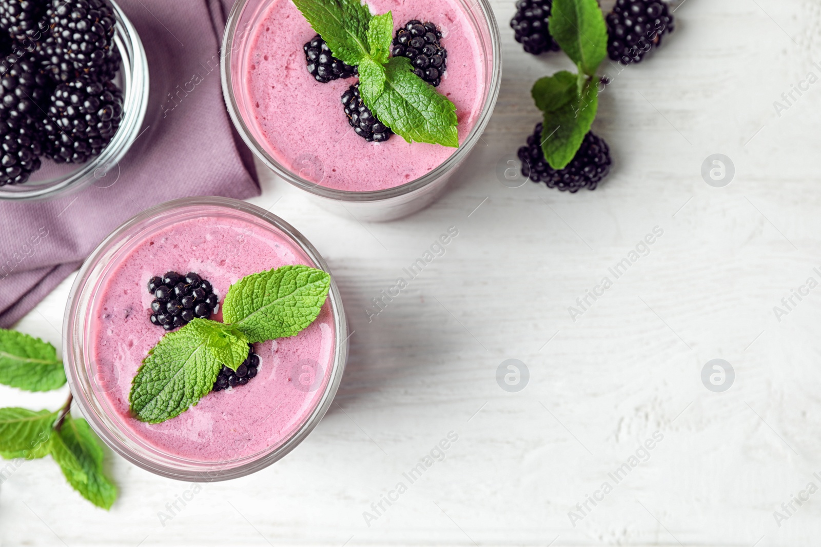 Photo of Flat lay composition with glasses of delicious blackberry smoothie on white wooden table. Space for text