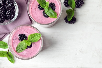 Flat lay composition with glasses of delicious blackberry smoothie on white wooden table. Space for text