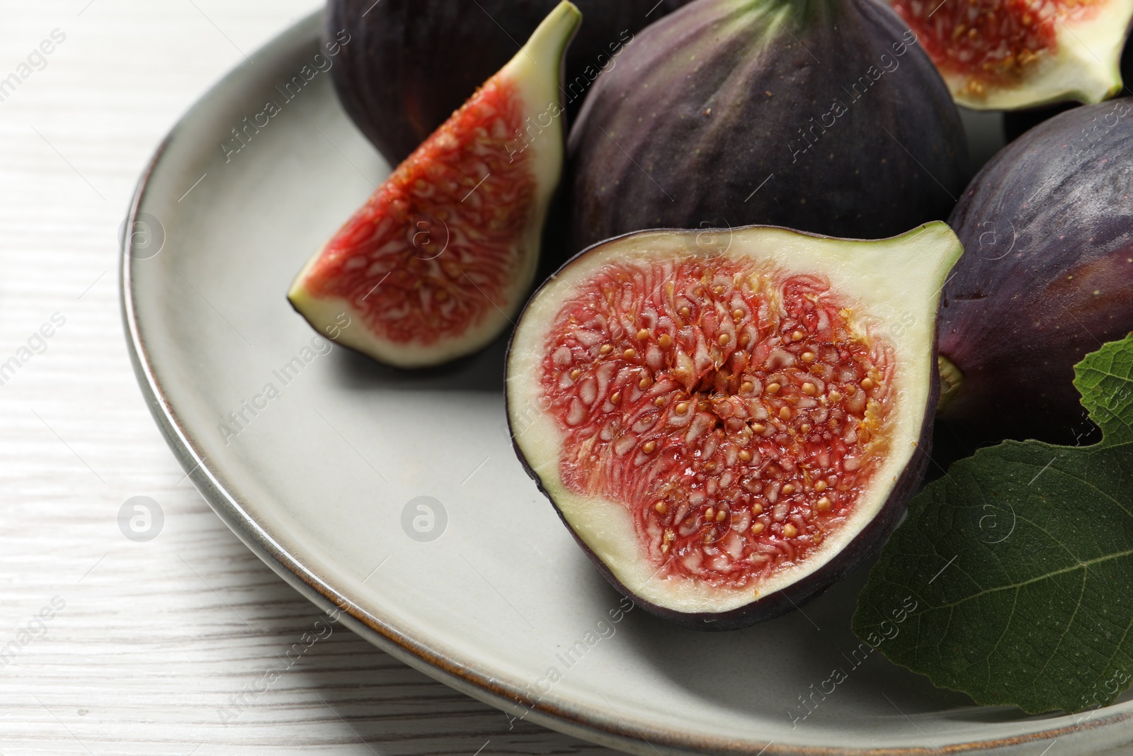 Photo of Whole and cut ripe figs with leaf on white wooden table, closeup