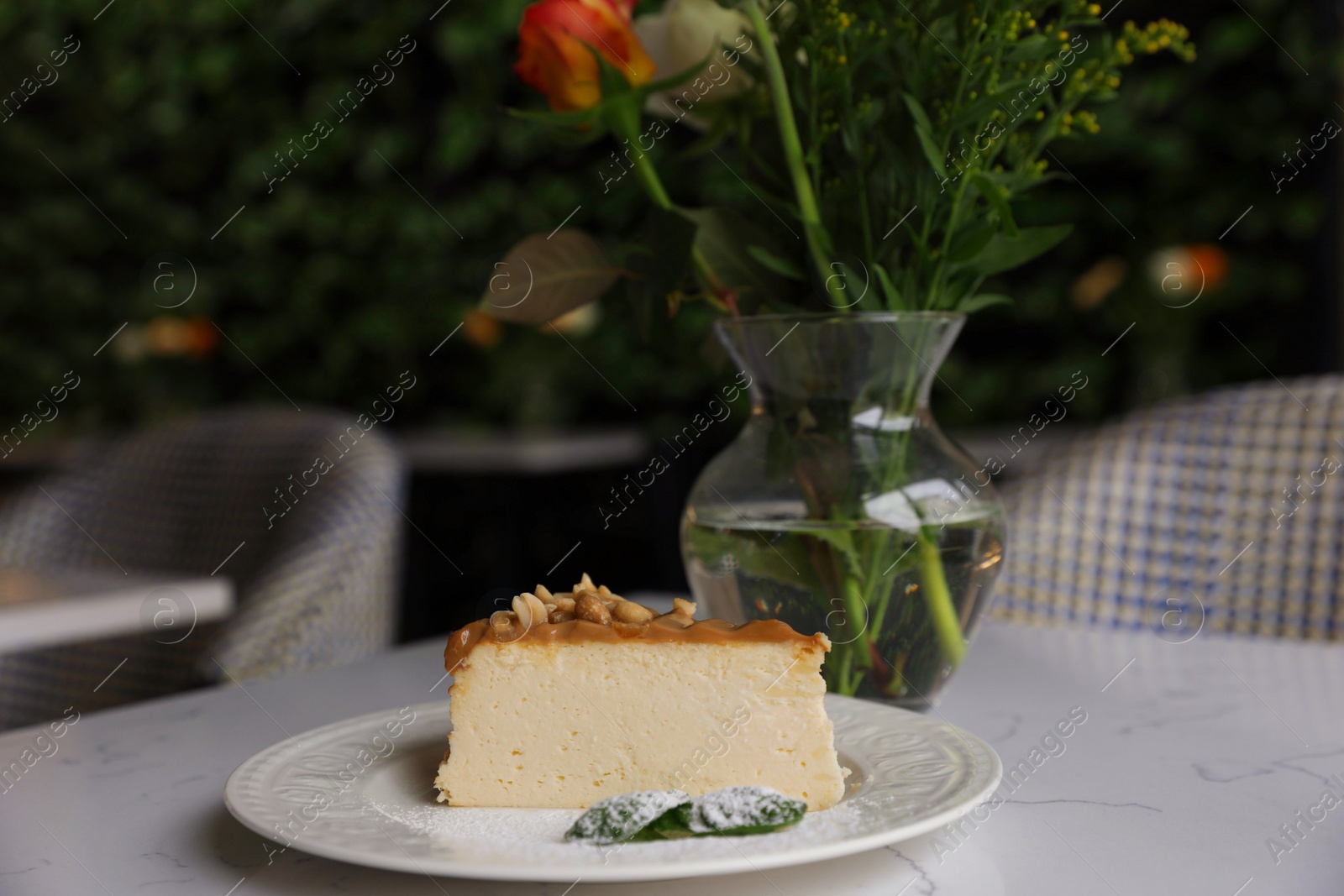 Photo of Tasty dessert and vase with flowers on white table in cafeteria