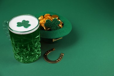 Photo of St. Patrick's day party. Green beer, leprechaun hat with gold, horseshoe and decorative clover leaves on green background. Space for text