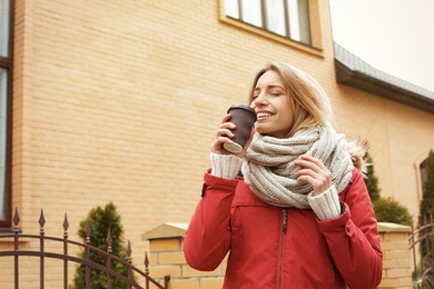 Young woman with cup of coffee walking outdoors. Space for text