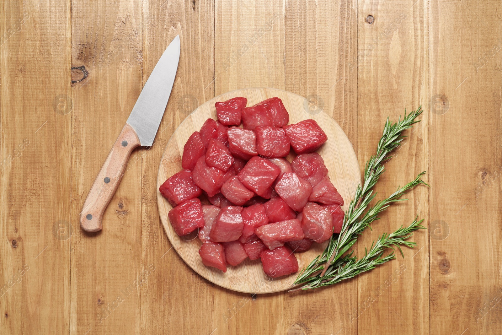 Photo of Cooking delicious goulash. Raw beef meat, rosemary and knife on wooden table, flat lay