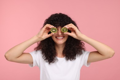 Photo of Woman covering eyes with halves of kiwi on pink background