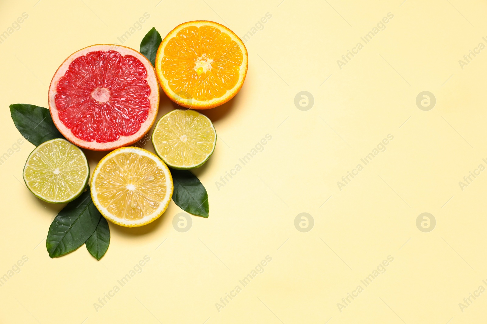 Photo of Different cut citrus fruits and leaves on beige table, flat lay. Space for text