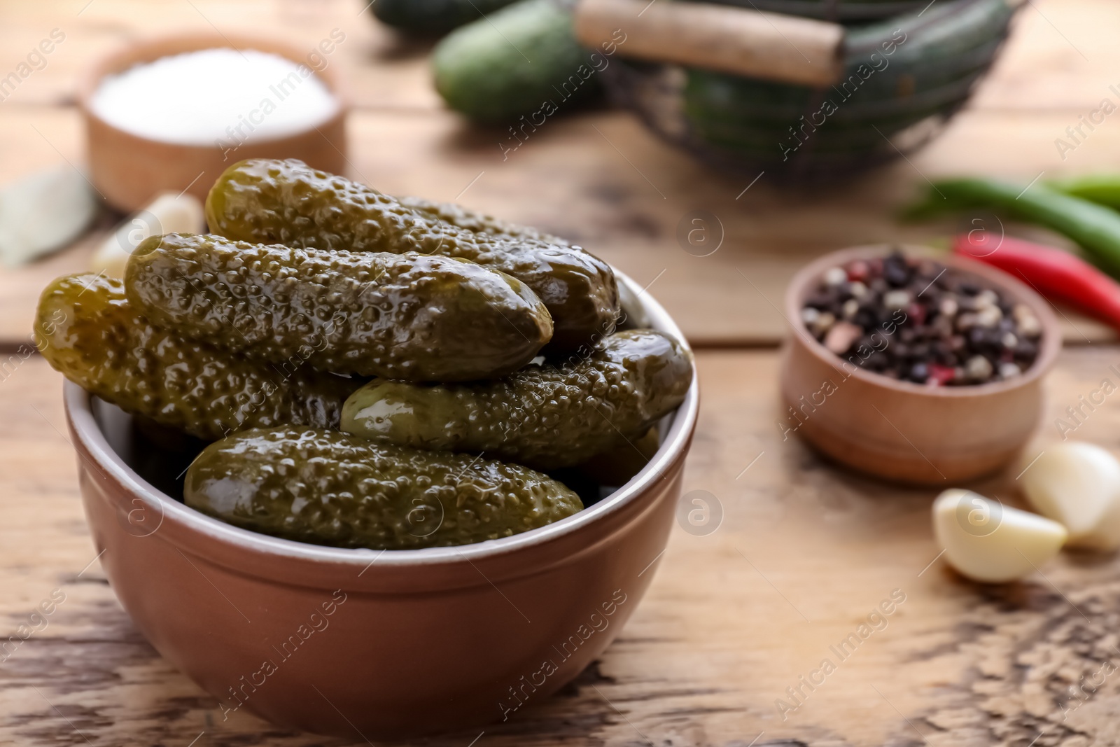 Photo of Bowl of pickled cucumbers and ingredients on wooden table, closeup