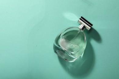 Luxury perfume in bottle on turquoise background, top view. Space for text