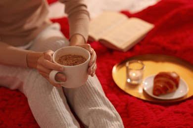 Photo of Woman with cup of drink relaxing on bed at home, closeup. Cozy atmosphere