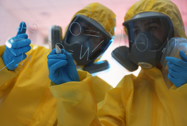 Photo of Scientists in chemical protective suits writing formula on glass board at laboratory. Virus research