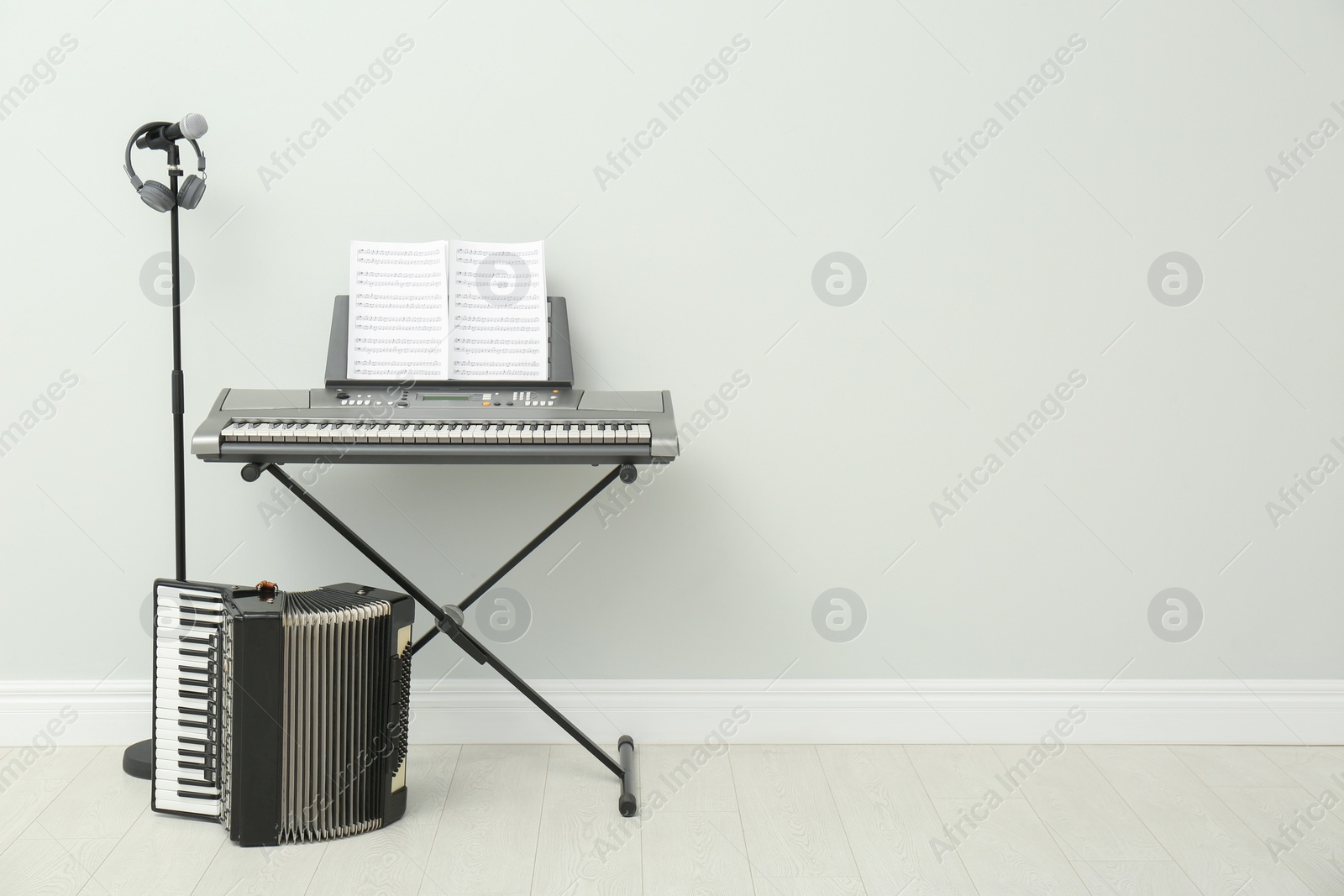 Photo of Electronic synthesizer, accordion and microphone near white wall indoors, space for text. Musical instruments