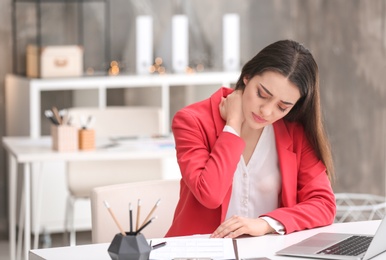 Photo of Young woman suffering from neck pain in office