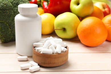 Photo of Dietary supplements. Bottle and bowl with pills near food products on light wooden table, closeup