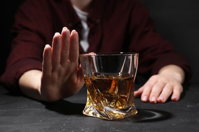 Photo of Alcohol addiction. Woman refusing glass of whiskey at dark textured table, closeup