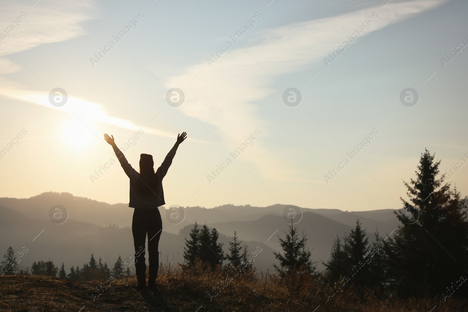 Photo of Silhouette of woman at sunrise in mountains, back view. Space for text