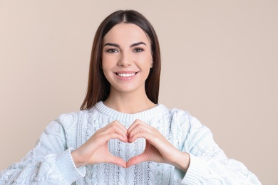 Photo of Portrait of young woman making heart with her hands on color background