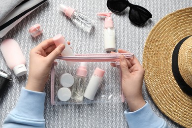 Photo of Cosmetic travel kit. Woman putting small bottle with personal care product into plastic bag on sofa, top view