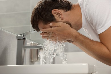 Photo of Handsome man washing face in bathroom, closeup