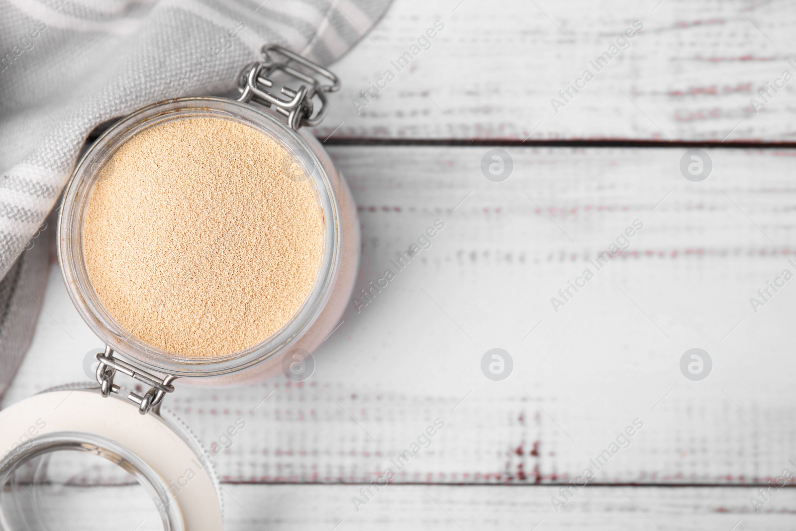 Photo of Granulated yeast in glass jar on white wooden table, top view. Space for text