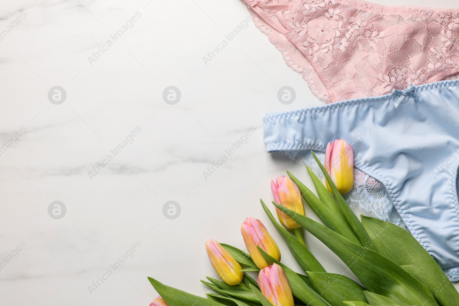 Photo of Elegant women's underwear and beautiful tulips on white marble background, flat lay. Space for text