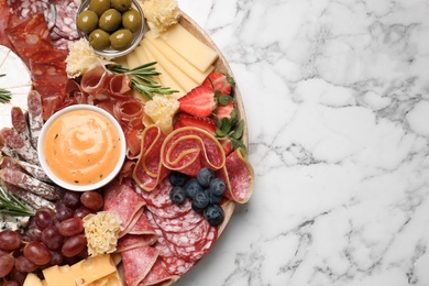 Photo of Wooden plate with different delicious snacks on white marble table, top view. Space for text