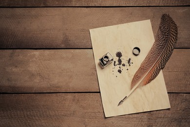 Photo of Feather pen, inkwell and vintage parchment with ink stains on wooden table, top view. Space for text