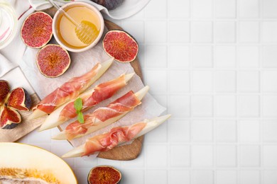 Photo of Tasty melon, jamon and figs served on white tiled table, flat lay. Space for text